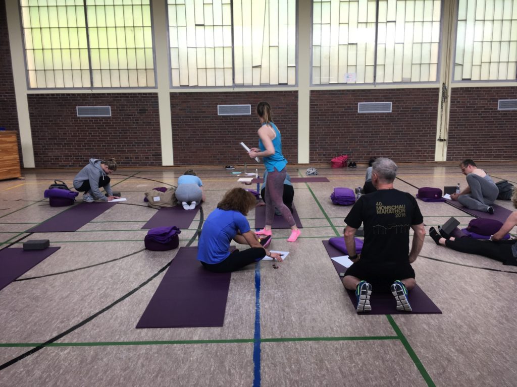 Yogagruppe übt Balancehaltungen in einer Turnhalle