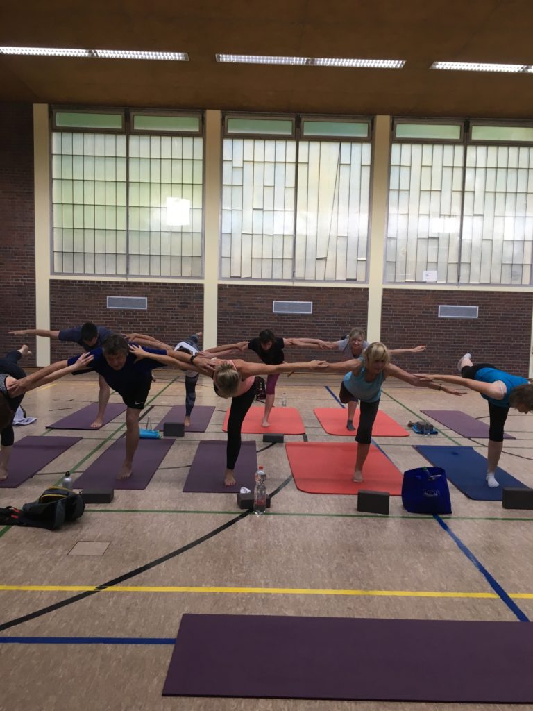 Yogagruppe übt Balancehaltungen in einer Turnhalle