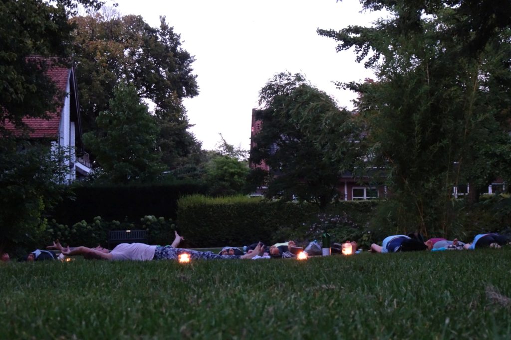 Yogagruppe auf der Wiese in der Abenddämmerung, umgeben von Kerzen – Yoga-Sommernacht