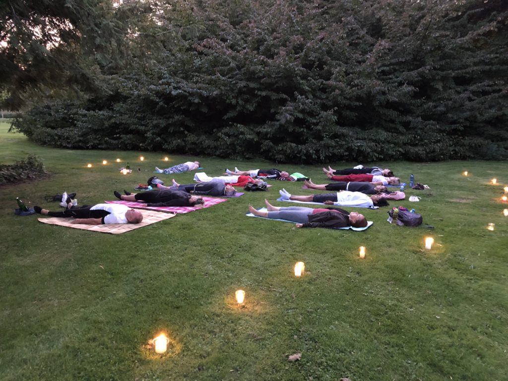 Yogagruppe auf der Wiese in der Abenddämmerung, umgeben von Kerzen – Yoga-Sommernacht