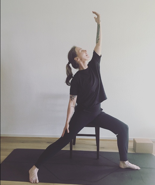 Bianka Polzius zeigt die Kriegerhaltung mit Stuhl als Hilfsmittel – Yoga für Senioren