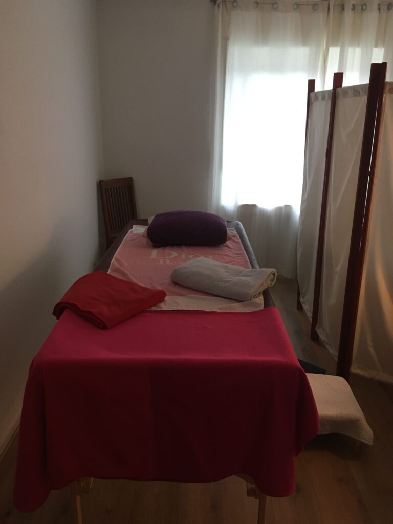 Massageliege mit roter Decke im Behandlungsraum für ayurvedische Massagen